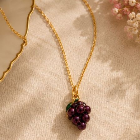Primer plano de un colgante de encanto de uva dorada sin deslustre en una cadena, perfecto para exhibiciones de catálogos de joyería al por mayor.