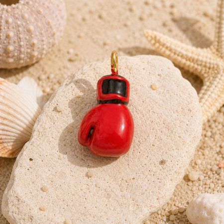 Close-up de um charm de esmalte de luva de boxe vermelha em uma pedra, ilustrando a construção durável e à prova d'água para compradores por atacado.