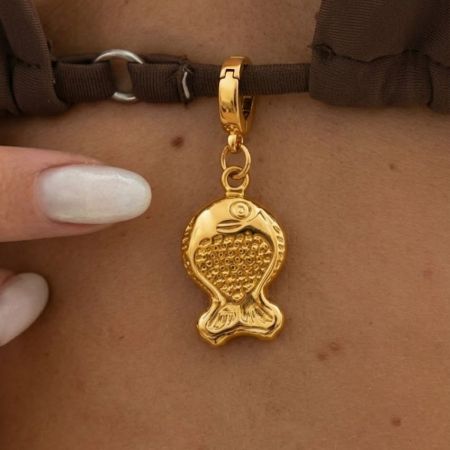 Primer plano de un encanto de pez de oro sujetado a una tira de bikini marrón, demostrando hardware personalizado funcional para ropa de resort.
