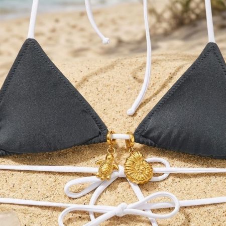 Encantos de tortuga y concha de oro adjuntos a un top de bikini negro sobre arena, ilustrando acentos decorativos premium para trajes de baño.