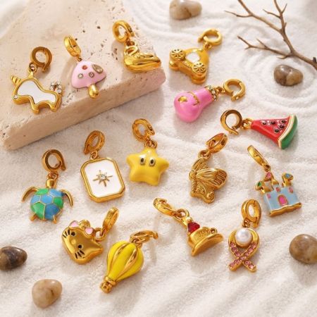 Péndulos de esmalte chapados en oro de 18K variados esparcidos sobre arena blanca, adecuados para la obtención de accesorios de moda de verano.