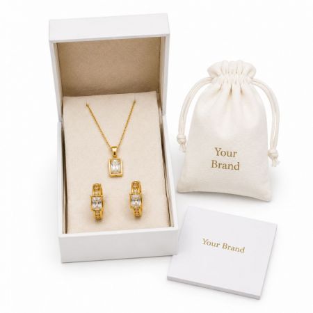 Emerald-cut CZ gold pendant necklace and hoop earrings in custom branded boxes for B2B jewelry wholesale.