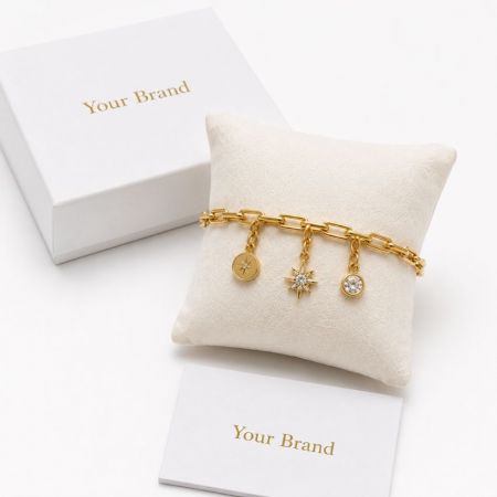 Gold chain charm bracelet with star and CZ pendants on display pillow with custom brand packaging wholesale.