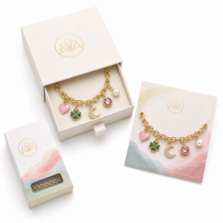 Gold fashion charm bracelet with pink enamel heart and green clover charms, complete with high-end retail packaging.
