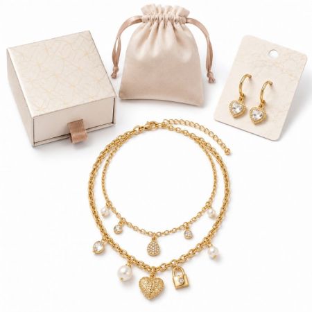 Layered gold chain necklace with padlock and heart charms, presented with retail packaging and hoop earrings.
