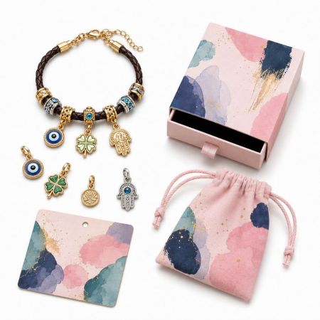 Braided leather evil eye charm bracelet with hamsa and four-leaf clover pendants, featuring wholesale display packaging.