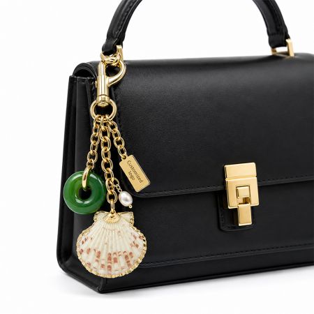 Hochwertige schwarze Lederhandtasche, dekoriert mit einem individuellen Logo-Muschel- und Jade-Anhänger, goldener Ketten-Taschenanhänger.