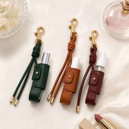 Green, brown, and burgundy leather lip balm keychain holders displayed on silk fabric for luxury fashion accessory wholesale.