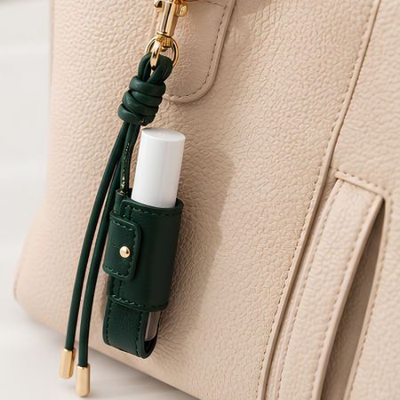 Forest green leather lip balm holder keychain attached to a handbag as a stylish cosmetic accessory charm.