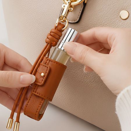 Hand inserting a travel spray bottle into a brown PU leather keychain holder attached to a tote bag.