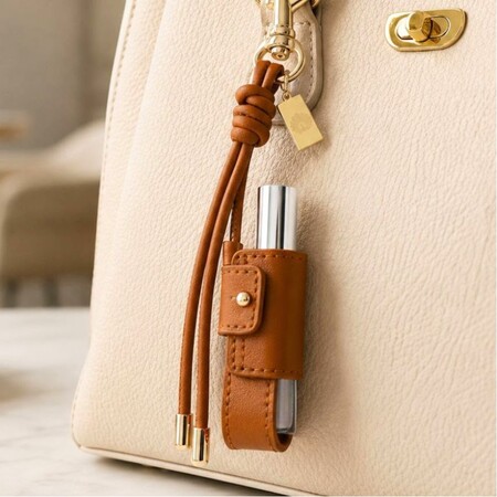 Brown leather lip balm keychain charm clipped on a luxury leather handbag for stylish, convenient carry.