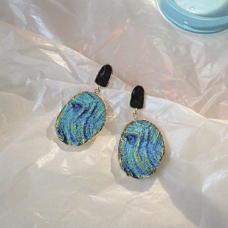 Close-up of a drop earring with an iridescent abalone shell-inspired design and gold trim.