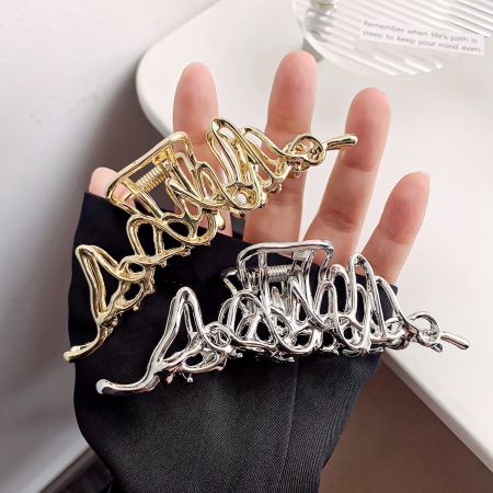 Clips de garra geométricos huecos de aleación metálica. - Un conjunto de clips de garra geométricos huecos de aleación metálica, mostrando los acabados dorado y plateado sostenidos por una mano enguantada.