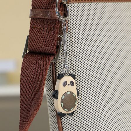 A cute wooden panda keychain hanging from a stylish handbag, perfect as a bag charm.
