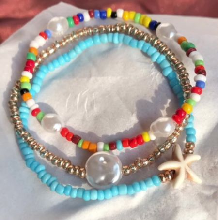 Close-up of three colorful beaded bracelets, showcasing a mix of gold, clear, and colored beads, highlighted by a starfish charm.
