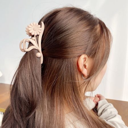 Eine Frau mit einem Pferdeschwanz, gestylt mit einer großen beigen Gänseblümchen-Haarspange.