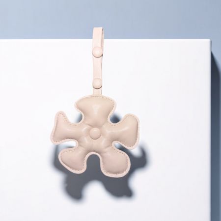 Un elegante llavero de cuero beige que presenta una forma única de trébol de cuatro hojas.