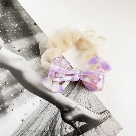 A chic beige scrunchie featuring an elegant purple acetate bow.