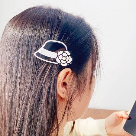 Una clip per capelli a forma di cappello chic in bianco e nero con un elegante accento floreale, perfetta per un look sofisticato.
