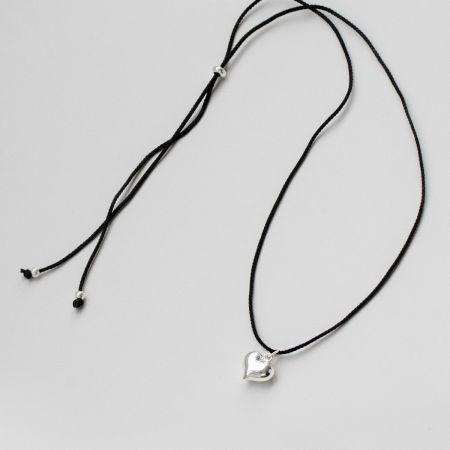 Vista completa del collar de cordón negro con el colgante en forma de corazón de plata.