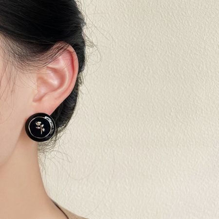 黒と金のスタッドピアスを着用した女性のクローズアップで、そのエレガントなデザインを紹介しています。