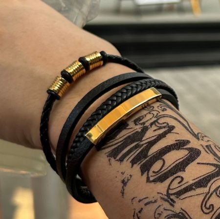 En samling av svarta PU-läderarmband med eleganta guldfärgade accenter, som visar olika stilar.