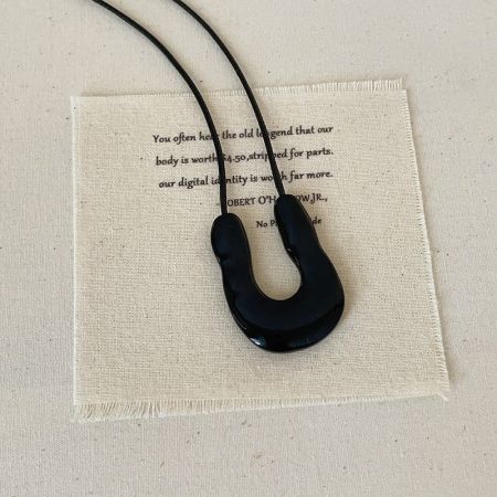 Black Cord U Shape Necklace Minimalist Pendant Statement Fashion Brass Jewelry Wholesale - A minimalist black U-shaped pendant on a black cord, displayed on a fabric background, representing modern statement fashion brass jewelry for wholesale.