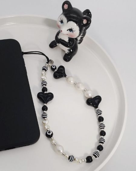 Close-up of a black and white beaded phone charm strap with a cute cat figurine, displaying the detailed craftsmanship.