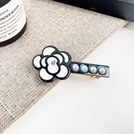 Vista dettagliata di una clip per capelli a forma di camelia con petali bianchi contornati di nero e un gambo di quattro eleganti perle.