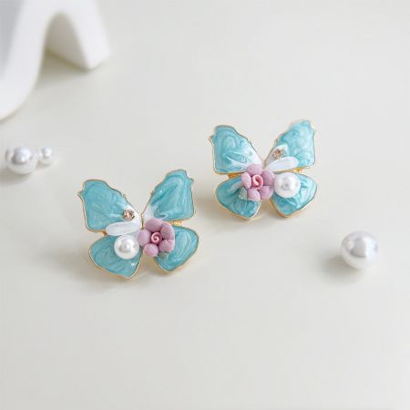 Boucles d'oreilles en forme de papillon en perles faites à la main en émail bleu plaqué or en gros (5 paires) - Une paire de boucles d'oreilles en forme de papillon en émail bleu plaqué or avec des détails délicats en perles et floraux sur un fond blanc propre.