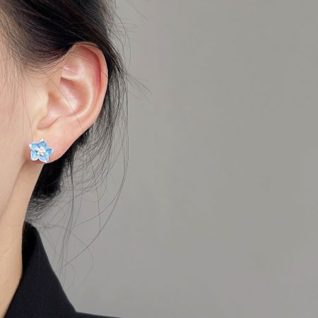スケールとスタイルを示すために、薄い青の花柄スタッドイヤリングを着用したモデル。