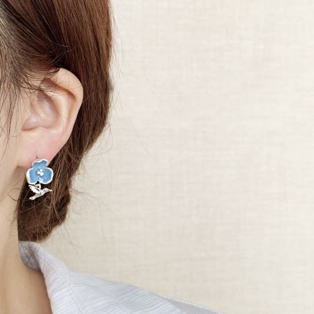 青いエナメルの花のイヤリングに銀の鳥のチャームをつけた女性のクローズアップ。