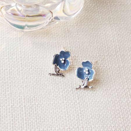 青いエナメルの花と銀のハチドリのチャームを特徴とするイヤリングのペア。