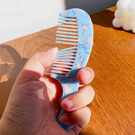 A hand holding a stylish blue and white marbled wide-tooth comb.