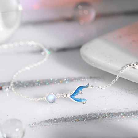 Un délicat collier en argent avec un pendentif en forme de baleine bleue et une perle opalescente.
