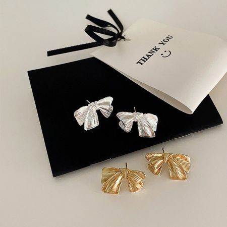 Orecchini a forma di fiocco in argento e oro presentati in una elegante scatola nera per gioielli.
