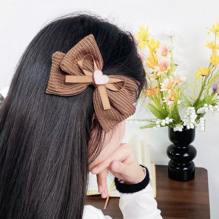 Detailed view of a brown knitted bow hair clip featuring a delicate heart charm.