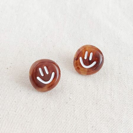 Scatto dettagliato degli orecchini a forma di faccina sorridente marrone lucidi, che mostrano la finitura del materiale.