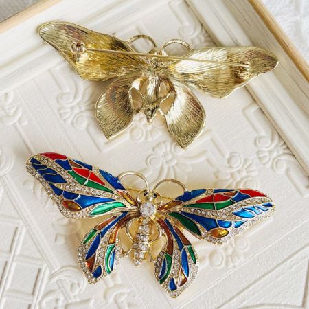 Un paio di spille a forma di farfalla che mostrano diverse variazioni di colore e disposizioni di pietre.