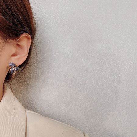 青と紫の石をあしらった金メッキの蝶のスタッドピアスを着けた女性のクローズアップ。
