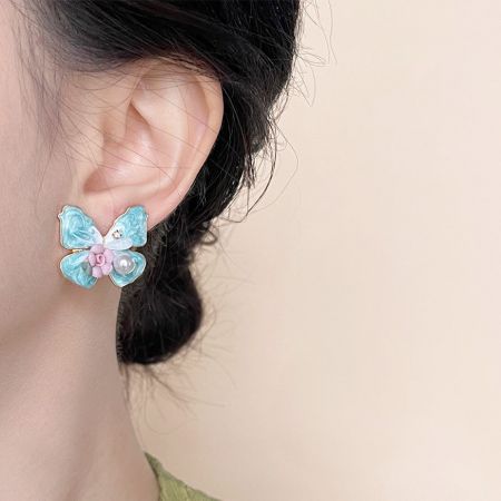 Vista detallada del esmalte azul, blanco y rosa en los pendientes de mariposa.
