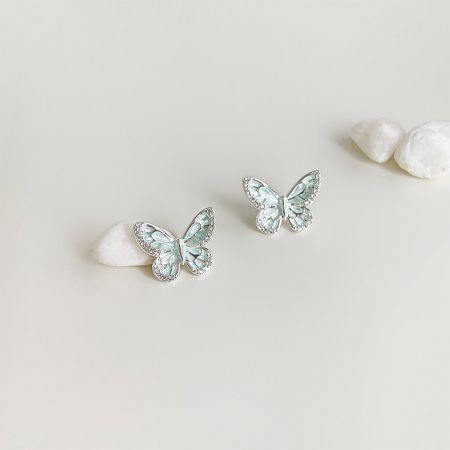 A pair of mint green butterfly earrings with silver details on a neutral background.