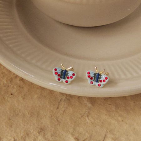 青いボディと赤い点のある翼を持つ蝶のイヤリングの詳細な商品写真。