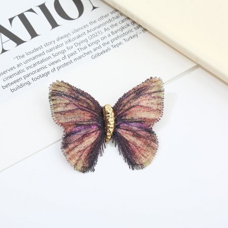 Vista detalhada do broche de borboleta multicolorido com tons de ouro, roxo, rosa e bege.