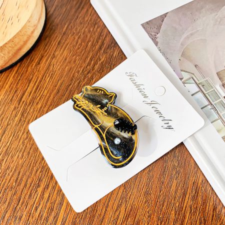 金色の魚の骨と真珠のアクセントが付いた黒いアセテート製の猫型ヘアクリップのクローズアップ。
