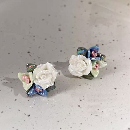 白いバラと緑の葉を特徴とする陶器の花のイヤリングの詳細ビュー。