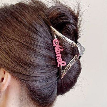 Een vrouw met een bun-haarstijl die een chique haarclip met gouden letters draagt.