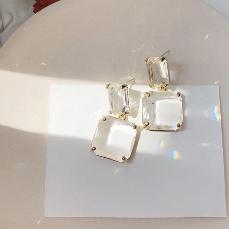 ディスプレイカードに載った金のセッティングの四角いカットの宝石イヤリングの詳細ビュー。