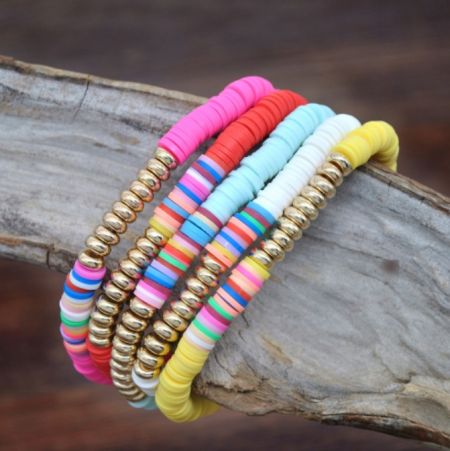 Detailed view of the colorful polymer clay and gold bead bracelets arranged artistically on natural driftwood.