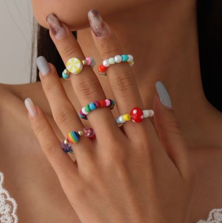 Primo piano di una mano che indossa più anelli di perline colorate, che mostrano uno stile popolare della collezione Primavera/Estate.
